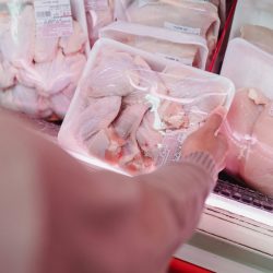 A shopper selects packaged chicken from a grocery store meat section.